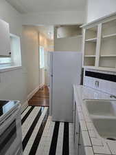 Kitchen with decorative backsplash, white appliances, baseboards, tile counters, and a sink