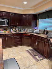 Kitchen with stainless steel microwave, a sink, ornamental molding, recessed lighting, and dark brown cabinetry