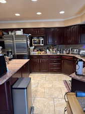 Kitchen featuring dark brown cabinets, ornamental molding, stainless steel appliances, and light stone countertops