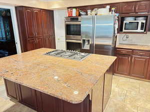 Kitchen with stainless steel appliances, light stone counters, and a center island