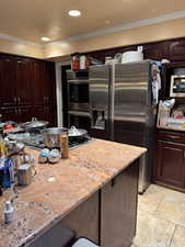 Kitchen featuring dark brown cabinets, ornamental molding, light stone countertops, and appliances with stainless steel finishes