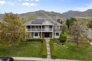 View of front facade with roof mounted solar panels, a mountain view, a front lawn, and brick siding