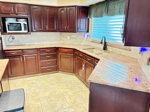 Kitchen with a sink, stainless steel microwave, tasteful backsplash, light stone countertops, and reddish brown cabinets