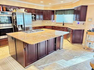 Kitchen featuring appliances with stainless steel finishes, a sink, crown molding, a center island, and light stone countertops