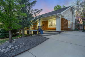 Property exterior at dusk with fence, covered porch, and a shingled roof