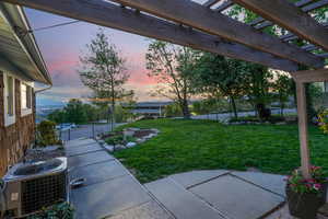 Yard at dusk with central air condition unit, a pergola, fence, and a patio area