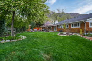 Rear view of property with a shingled roof, central AC, a mountain view, a patio area, and a lawn