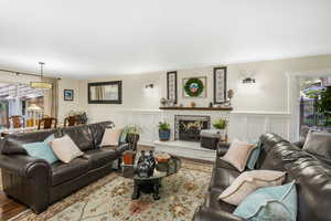 Living room with a decorative wall, a lit fireplace, wood finished floors, and a wainscoted wall