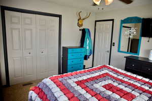 Carpeted bedroom featuring a ceiling fan, visible vents, and a closet