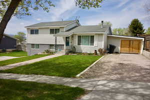 Split level home with fence, roof with shingles, driveway, and a front lawn