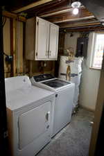 Clothes washing area featuring washer and clothes dryer, cabinet space, water heater, and electric panel