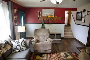 Living area with stairs, wood finished floors, baseboards, ceiling fan, and a wainscoted wall