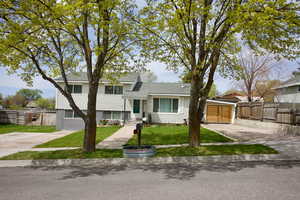Split level home with fence, roof with shingles, and a front lawn
