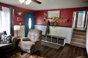 Living room featuring stairway, a wainscoted wall, a ceiling fan, and wood finished floors