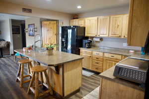 Kitchen with light brown cabinetry, a kitchen breakfast bar, a sink, and black fridge with ice dispenser