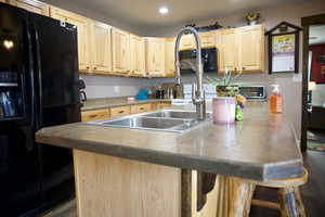 Kitchen featuring a breakfast bar, a sink, light brown cabinets, recessed lighting, and black appliances