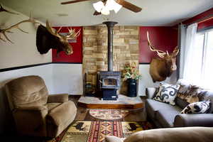 Living area featuring a ceiling fan, wainscoting, wood finished floors, and a wood stove