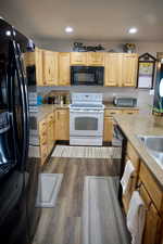 Kitchen featuring light countertops, light brown cabinetry, black appliances, and dark wood-type flooring