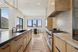 Kitchen featuring light brown cabinetry, a sink, light wood finished floors, stainless steel stove, and wall chimney exhaust hood