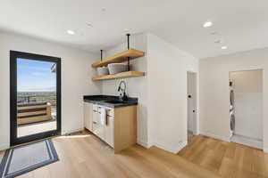 Bar with a sink, stacked washer and clothes dryer, recessed lighting, and light wood-style flooring