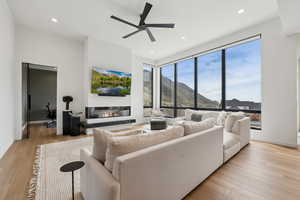 Living room with a glass covered fireplace, baseboards, ceiling fan, light wood-type flooring, and recessed lighting
