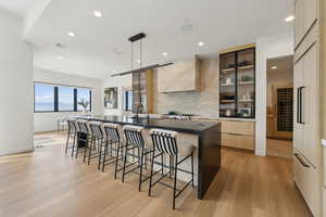 Kitchen featuring wall chimney range hood, light wood finished floors, a breakfast bar area, a spacious island, and modern cabinets