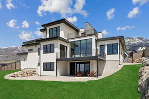 Rear view of house with stucco siding, a mountain view, a patio area, a balcony, and a yard
