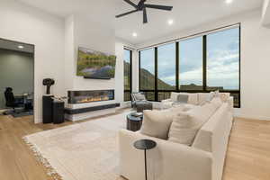 Living area with a glass covered fireplace, baseboards, ceiling fan, recessed lighting, and light wood-style flooring