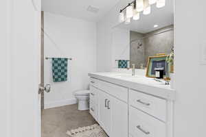 Bathroom featuring a tile shower, vanity, and toilet
