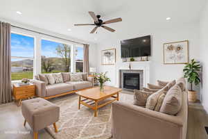 Living room with light wood-type flooring, ceiling fan, a fireplace with flush hearth, and recessed lighting