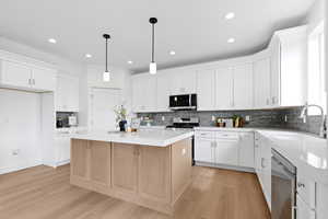 Kitchen with mitered edge quartz countertops, white cabinets, hardwood flooring, appliances with stainless steel finishes, and gray backsplash