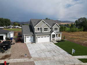 View of front of home with a shingled roof, concrete driveway, a mountain view, a front yard, and covered porch
