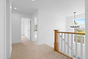 Hallway with light colored carpet, an inviting chandelier, recessed lighting, baseboards, and an upstairs landing