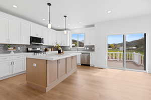Kitchen with mitered edge quartz countertops, white cabinets, hardwood flooring, appliances with stainless steel finishes, and gray backsplash