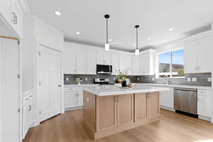 Kitchen with mitered edge quartz countertops, white cabinets, hardwood flooring, appliances with stainless steel finishes, and gray backsplash