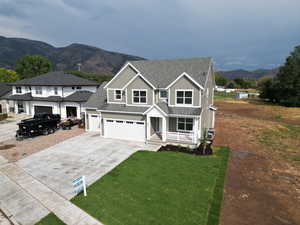 View of front facade with roof with shingles, a mountain view, driveway, a front yard, and covered porch