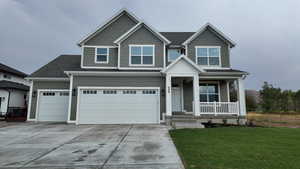View of front facade featuring concrete driveway, covered porch, and a front yard