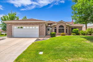 Single story home featuring an attached garage, a tile roof, a front lawn, brick siding, and concrete driveway
