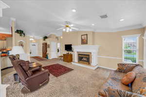 Living room featuring ceiling fan, visible vents, crown molding, a tiled fireplace, and baseboards
