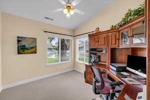 Office space with ceiling fan, visible vents, baseboards, lofted ceiling, and light carpet