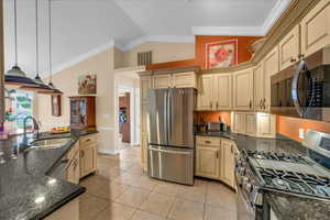 Kitchen featuring a sink, appliances with stainless steel finishes, cream cabinets, and vaulted ceiling