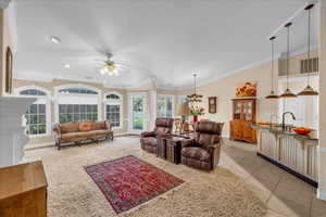 Living area featuring light tile patterned flooring, baseboards, ornamental molding, and ceiling fan with notable chandelier