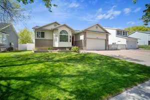 View of front of home with concrete driveway, an attached garage, fence, brick siding, and a front lawn