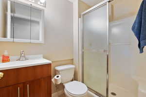 Bathroom featuring toilet, vanity, and a stall shower
