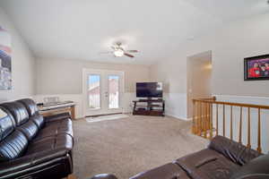 Carpeted living room featuring lofted ceiling, french doors, a ceiling fan, and a wainscoted wall