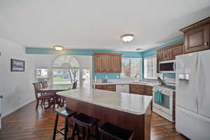 Kitchen featuring white appliances, a sink, dark wood-style floors, a center island, and a kitchen breakfast bar