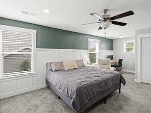 Carpeted bedroom featuring a wainscoted wall, a decorative wall, a textured ceiling, and visible vents