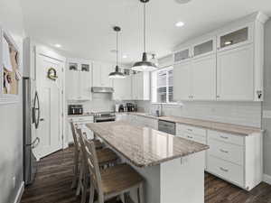 Kitchen with a breakfast bar area, a kitchen island, appliances with stainless steel finishes, under cabinet range hood, and dark wood-type flooring