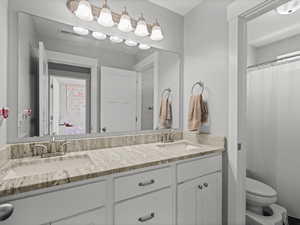 Bathroom with a sink, toilet, double vanity, and visible vents