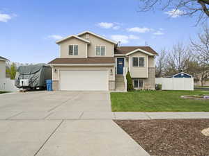 Multi-level home with driveway, a garage, brick siding, fence, and front lawn